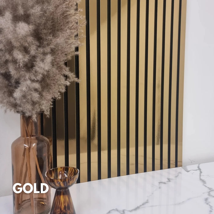 Decorative wall with gold and black slat wall panel, vase with dried plants on marble surface.